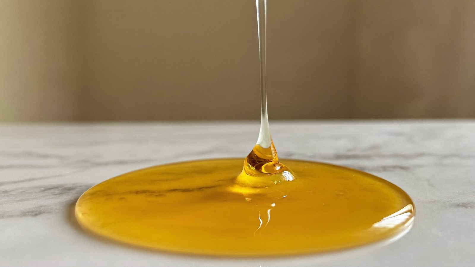 A dropper releasing golden tanning serum onto a marble bathroom counter