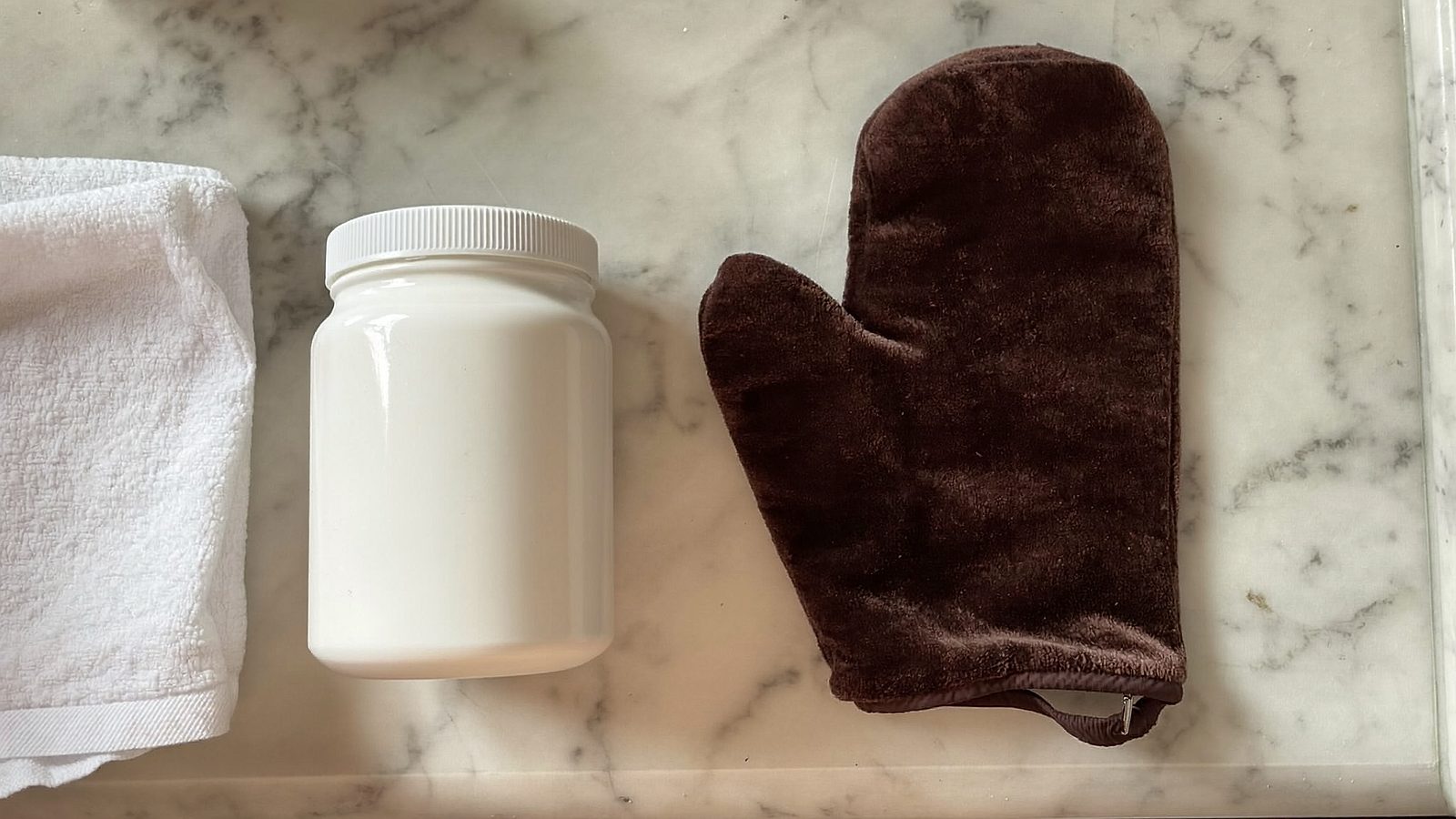 A tanning mitt and self tanner resting on a bright bathroom counter