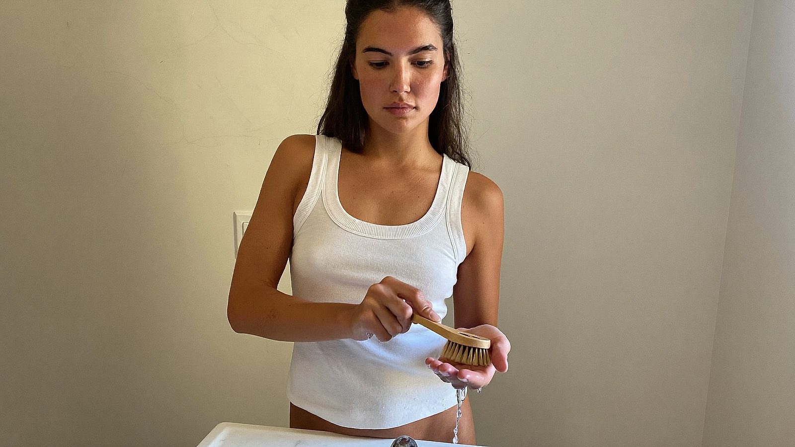 Woman scrubbing her palm with a small brush at a bathroom sink