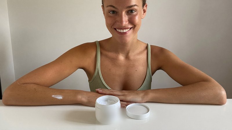 Woman smoothing white Soleau tanning cream onto her forearm at a bright bathroom counter