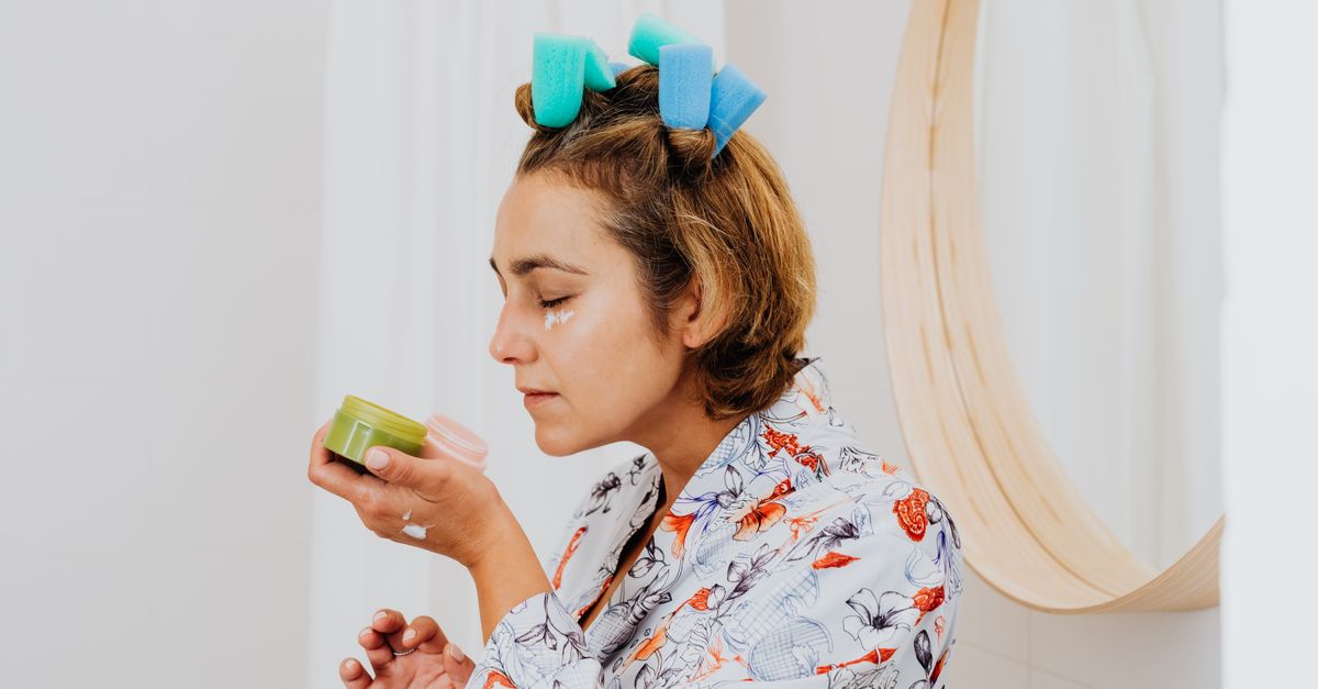 Woman with curlers testing a cream at her bathroom mirror