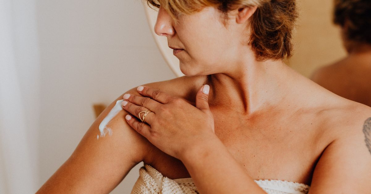 Woman smoothing cream onto her shoulder after a shower