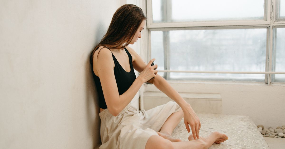 Woman applying lotion to her arm beside a bright window