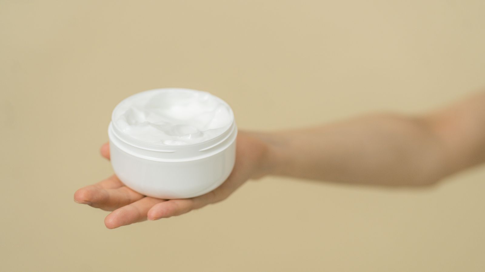 Hand holding an open jar of white cream