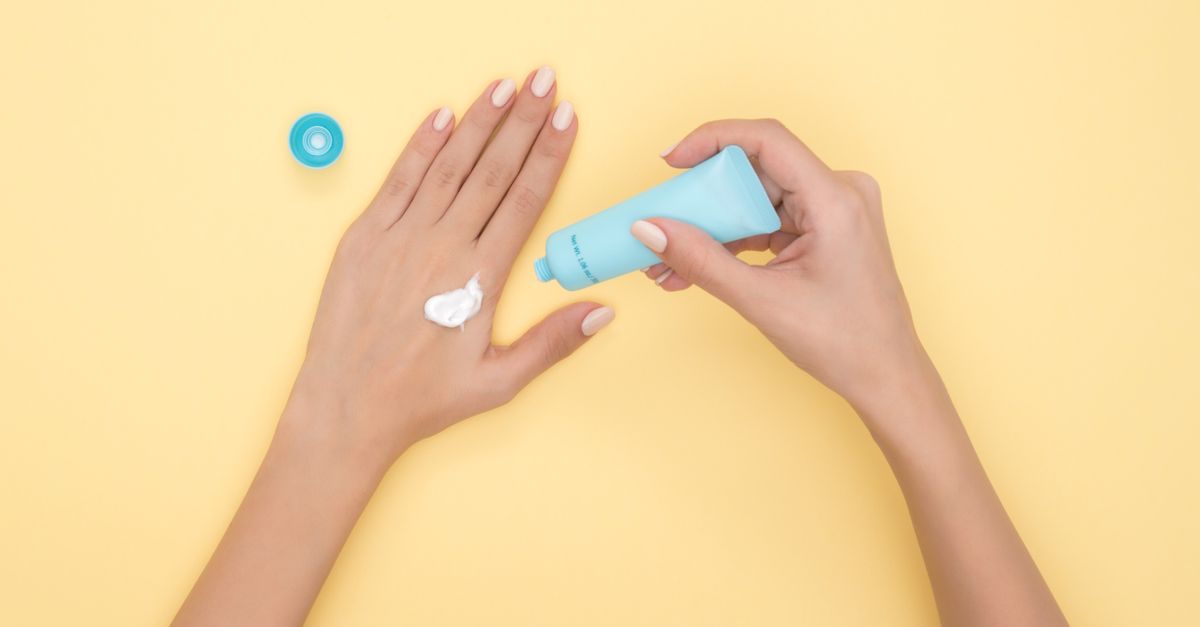 Hands squeezing moisturizer from a tube onto the back of a hand