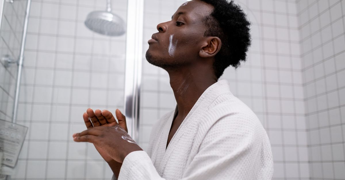 Man in a bathrobe applying cream to his face in the bathroom