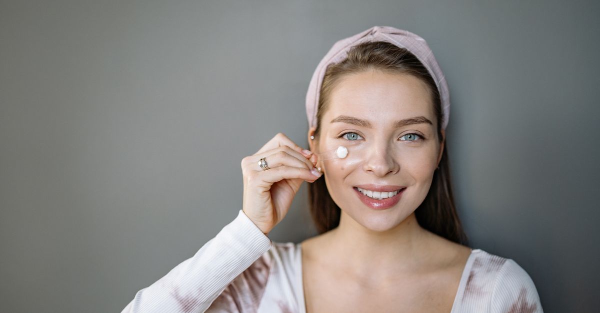 Smiling woman in a headband applying cream to her cheek