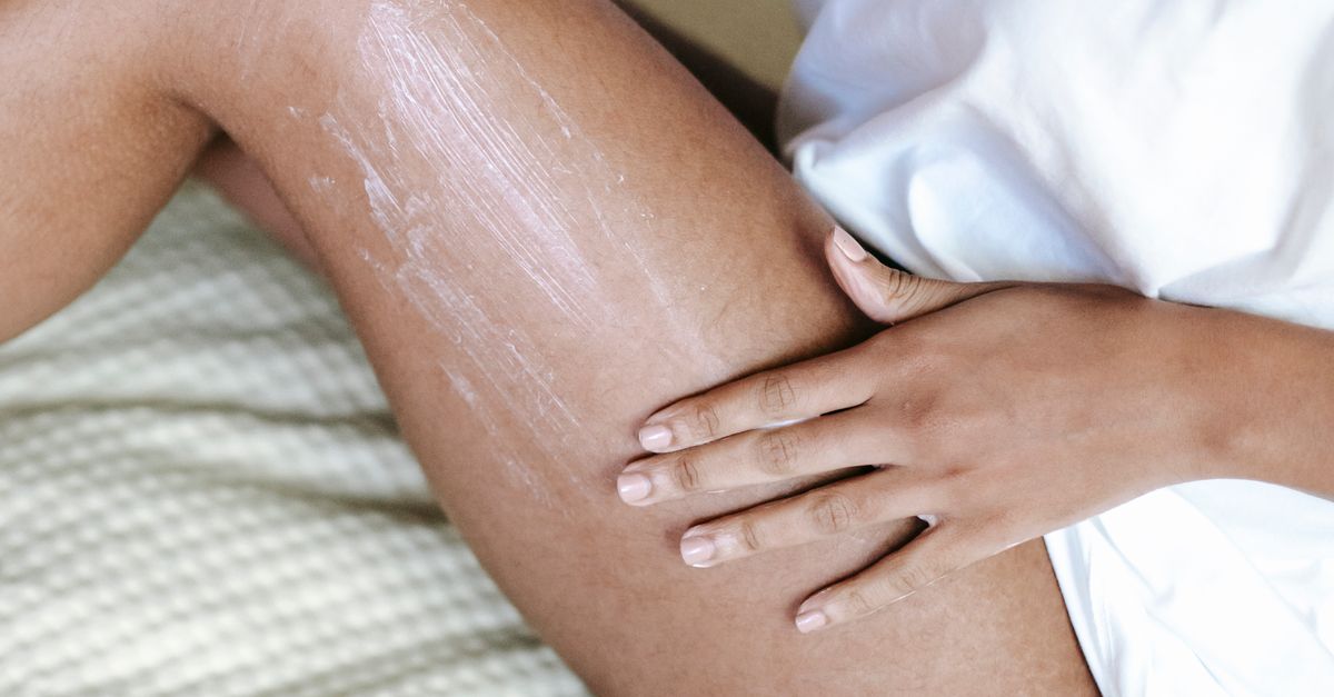 Woman spreading cream along her thigh while sitting on a bed