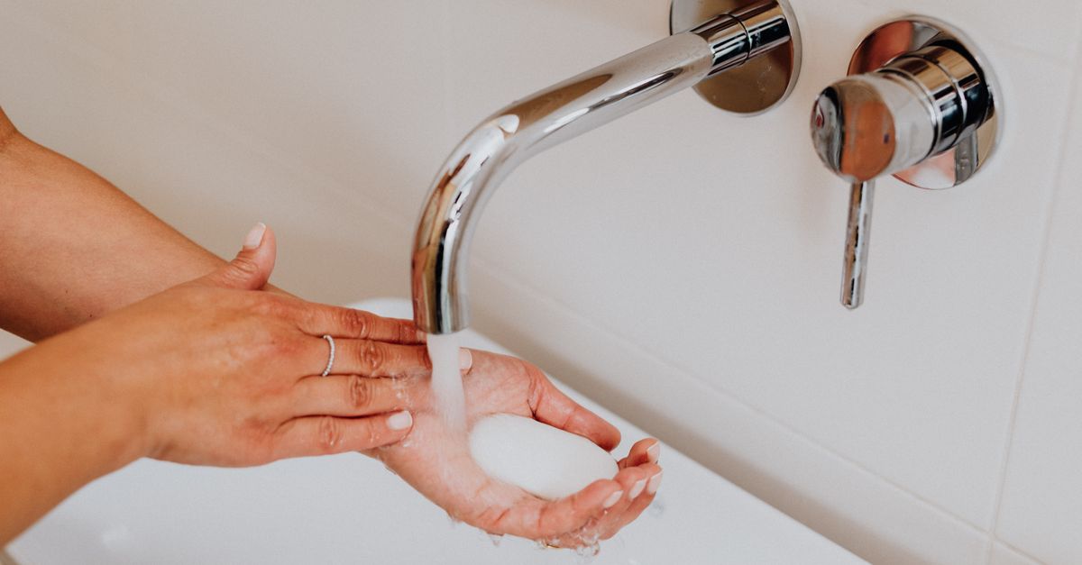 Hands lathering a bar of soap under running water