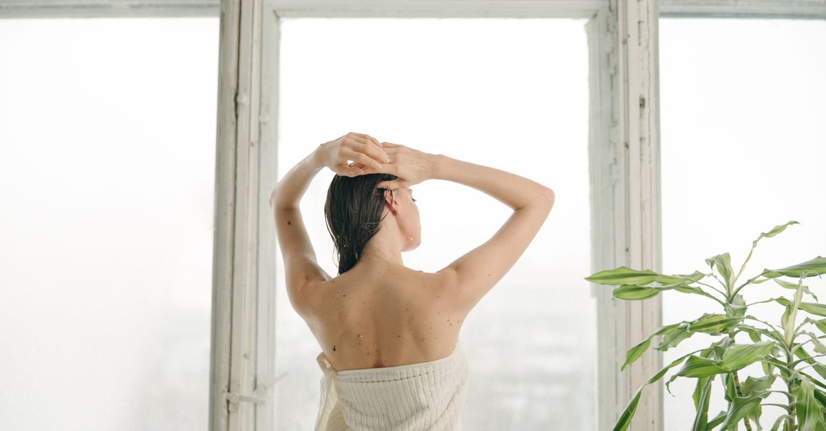 Woman wrapped in a towel showing her bare back by a window