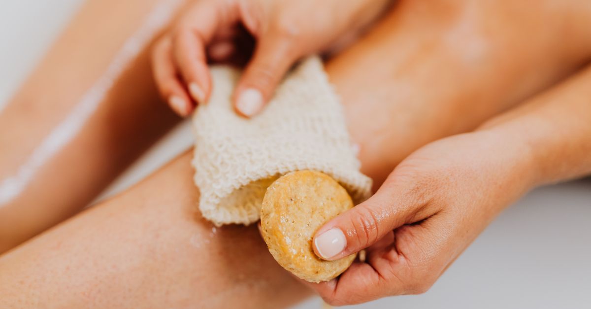 Hands holding an exfoliating mitt and soap over smooth legs