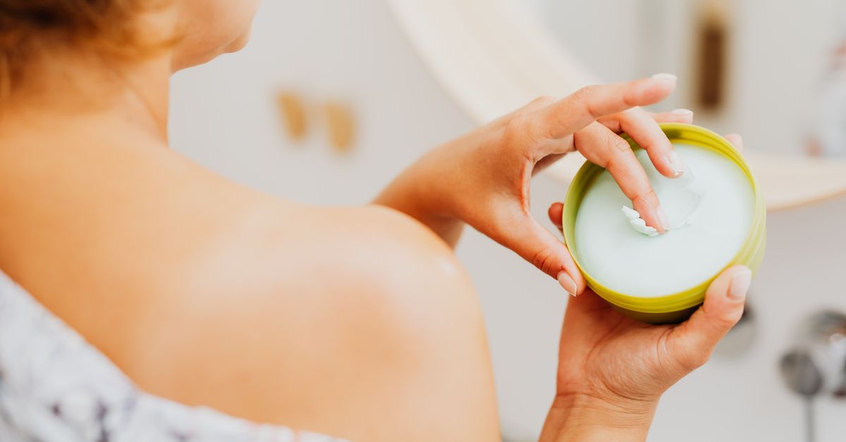 Woman scooping cream from a jar in her bathroom