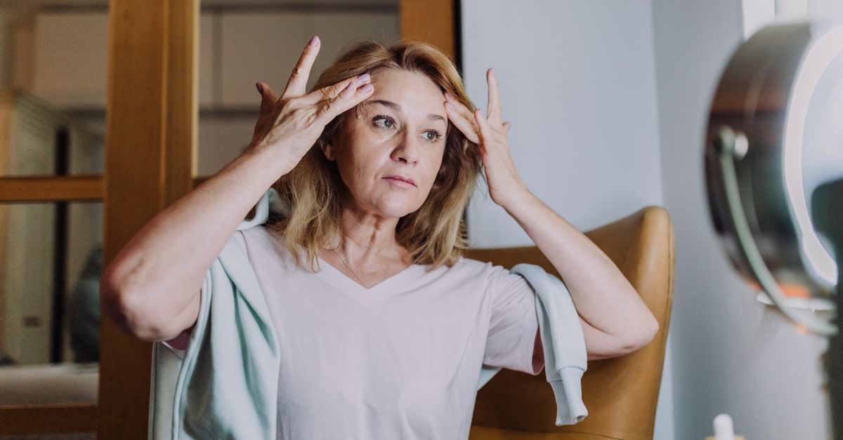 Mature woman massaging cream into her temples at her vanity