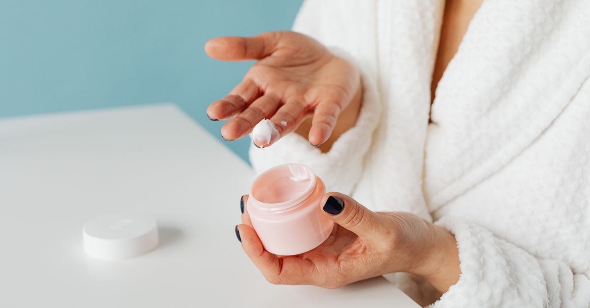 Woman in a robe scooping gentle cream from a jar