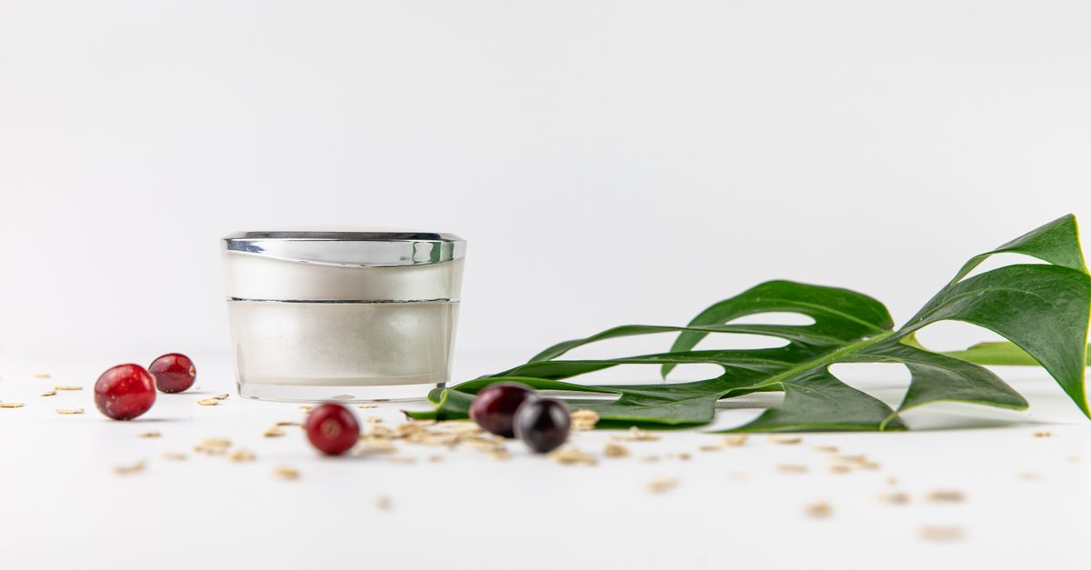 Cream jar beside green leaves and berries