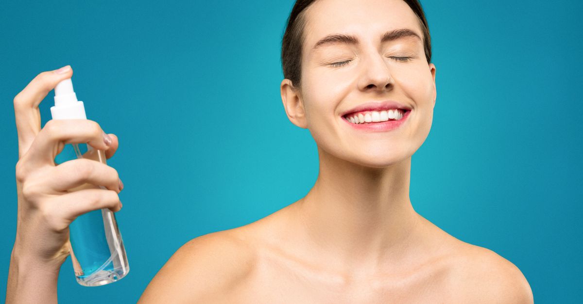 Smiling woman spraying a fine mist toward her face