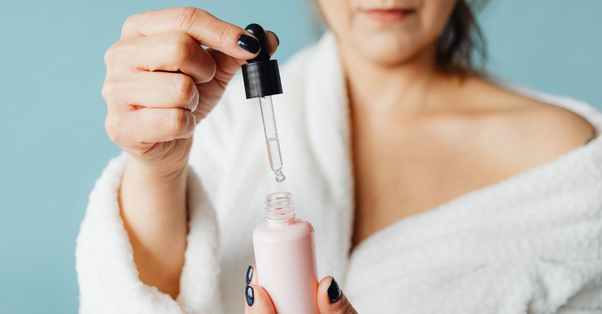 Woman in a robe holding a dropper over a serum bottle
