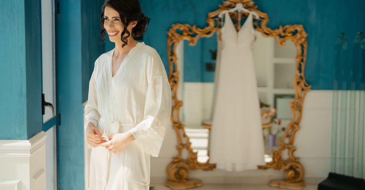 Bride in a robe smiling beside her wedding dress